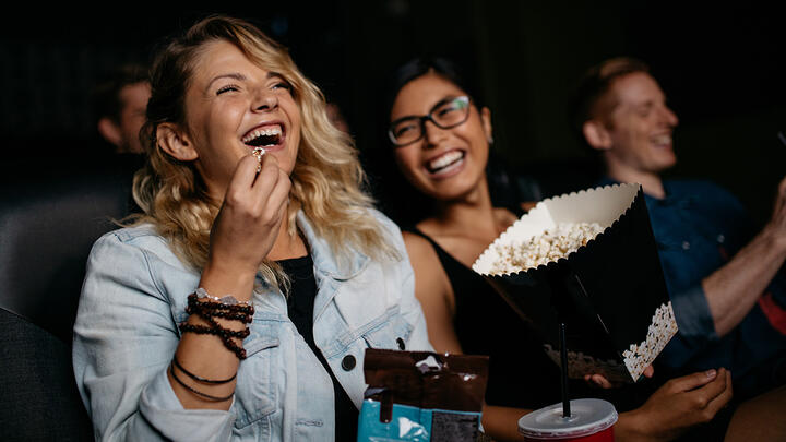 Three women having fun, eating popcorn in a movie theater